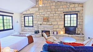 A cozy room with a stone wall, a fireplace, a bed, a sofa, and a TV. - Villa Maria Latchi in Latchi (Neo Chorio)