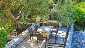 An outdoor patio with stone flooring, a marble table, wicker chairs, and a stone wall. - Villa Joanna in (Corfu)