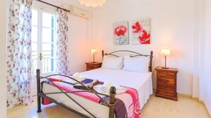 A bedroom with a bed, two bedside tables, a window with floral curtains, and two wall-mounted lamps. - Villa Joanna in (Corfu)