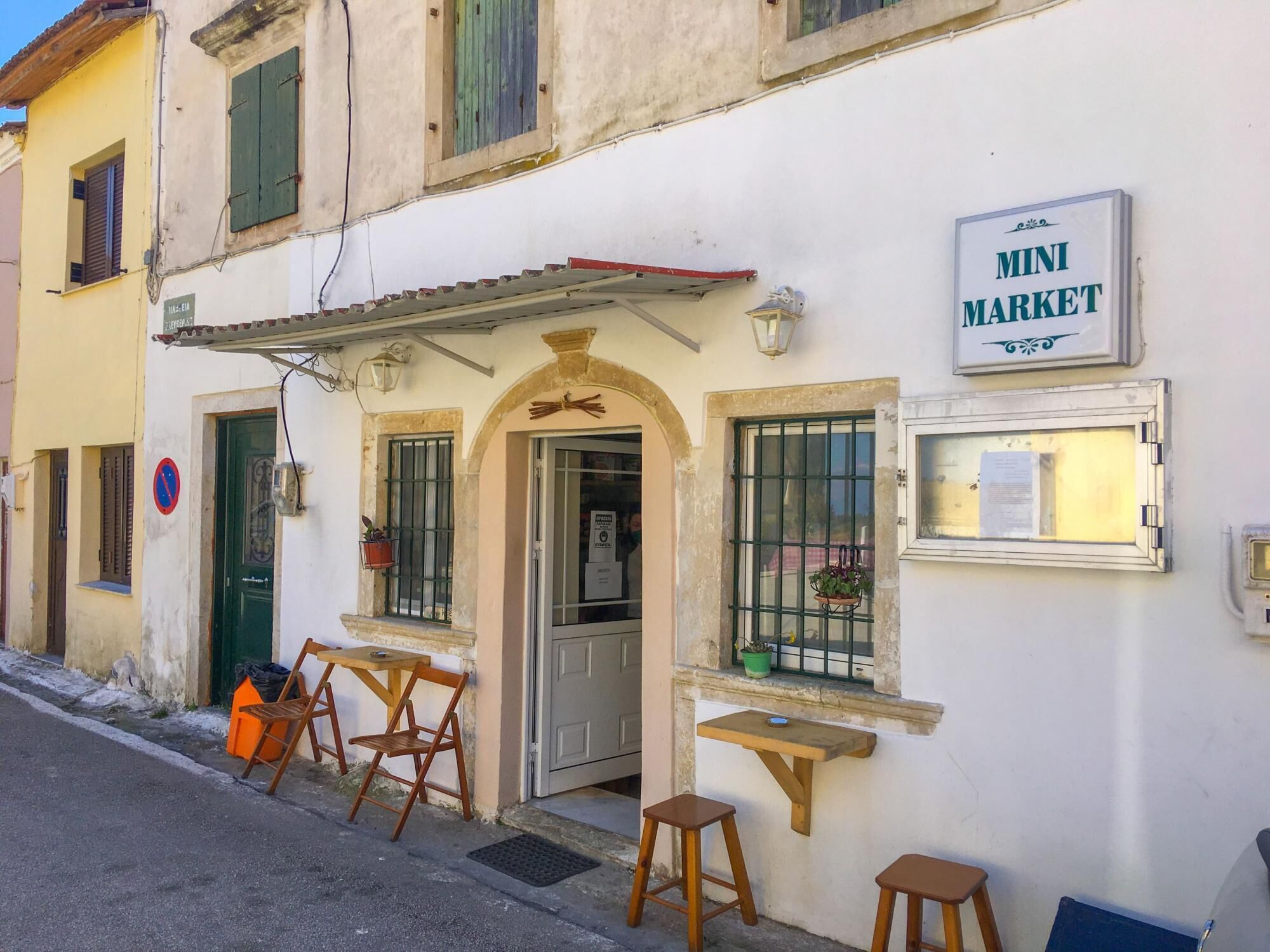 A building with a 'Mini Market' sign, a door, and a small outdoor seating area with tables and chairs.