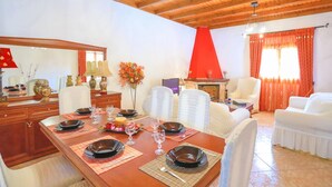 Uma sala de jantar com uma mesa de madeira posta para quatro pessoas, rodeada por cadeiras brancas.