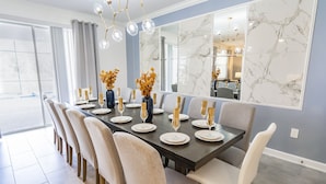 Une salle à manger avec un mur en marbre, une longue table dressée pour six personnes et un lustre.