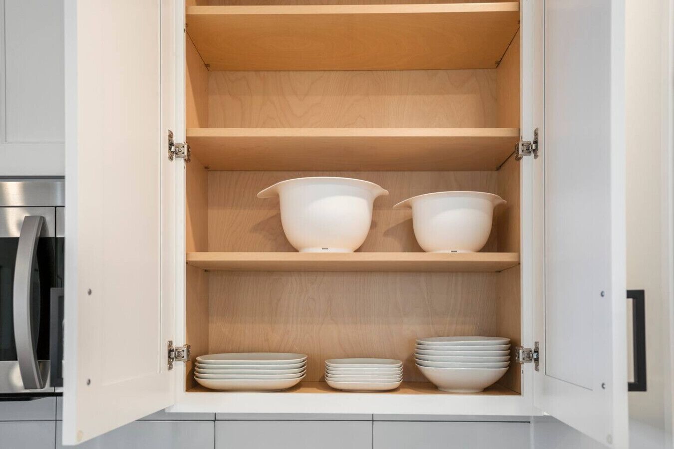 A kitchen cabinet with three shelves, each holding bowls and plates.