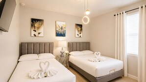 Ein Hotelzimmer mit zwei Betten, einem Fernseher, Kunstwerken an der Wand und einem Fenster mit Vorhängen.
