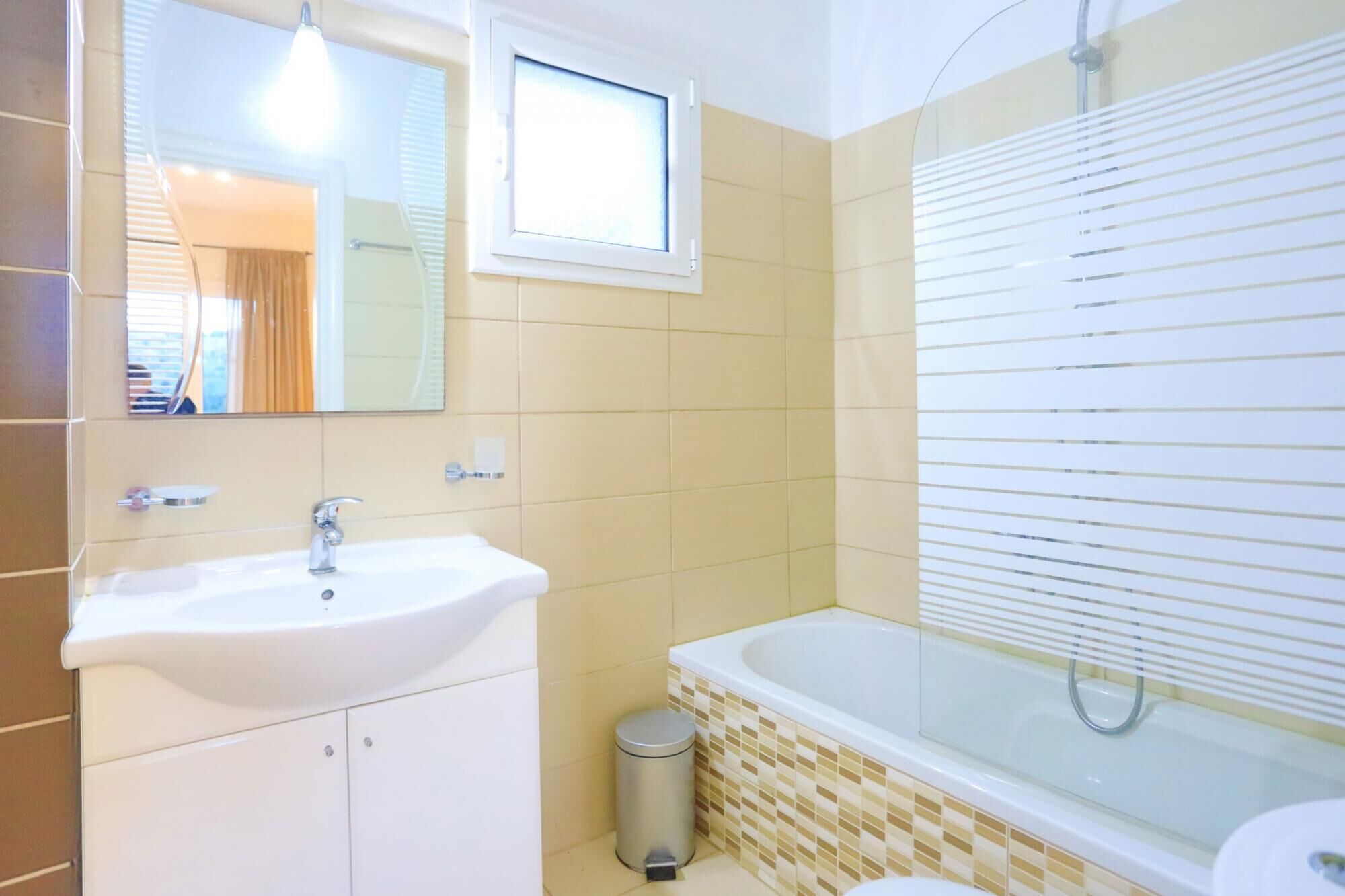 A bathroom with a white sink, a mirror, a window, a bathtub, and a toilet.