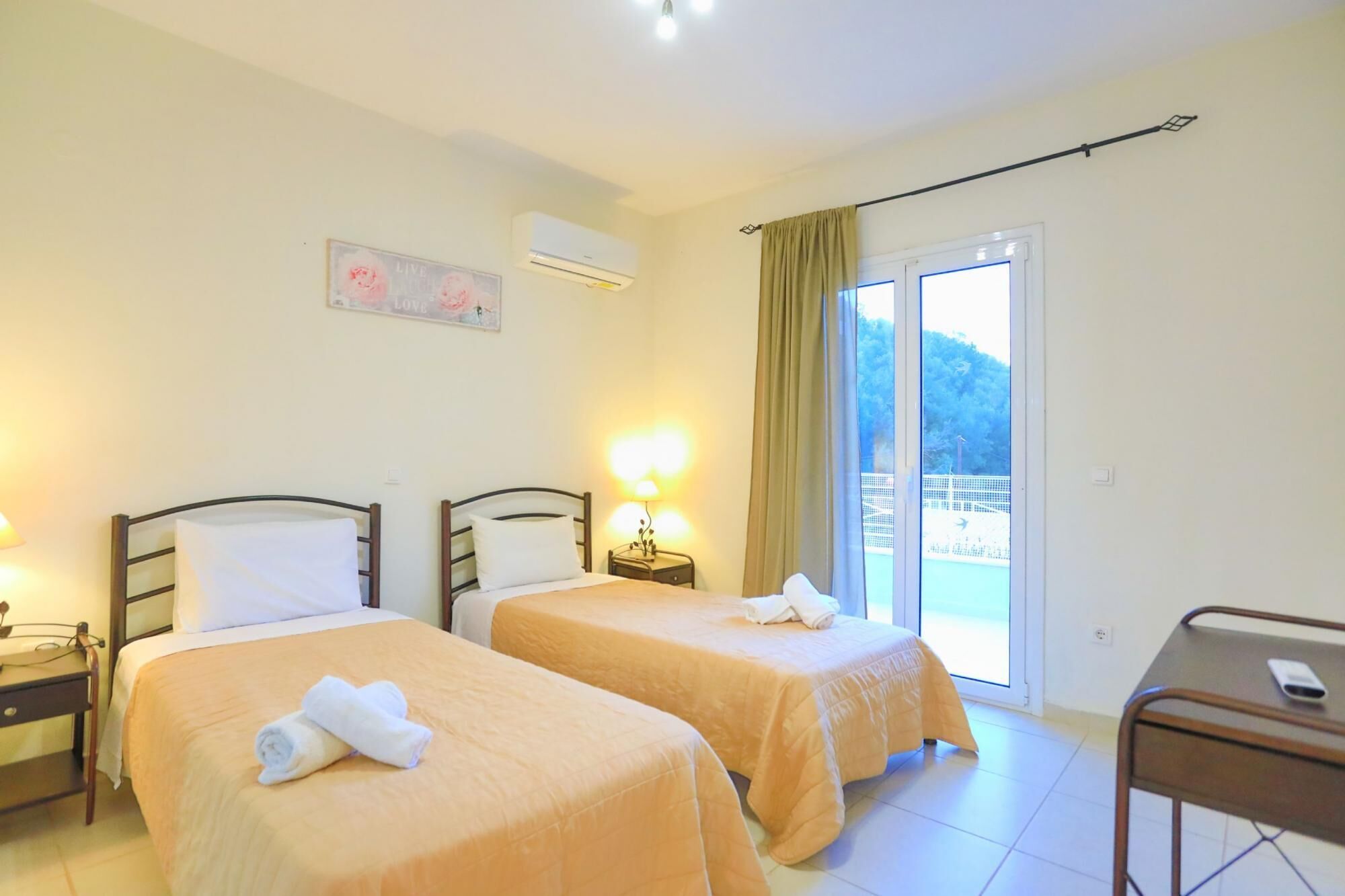 A hotel room with two beds, a small desk, and a balcony with a view.