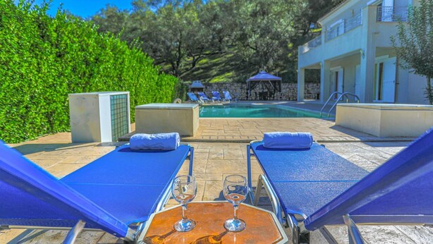 A poolside area with lounge chairs, a table with a glass, and a clear view of the pool. - Villa Anamari in (Corfu)