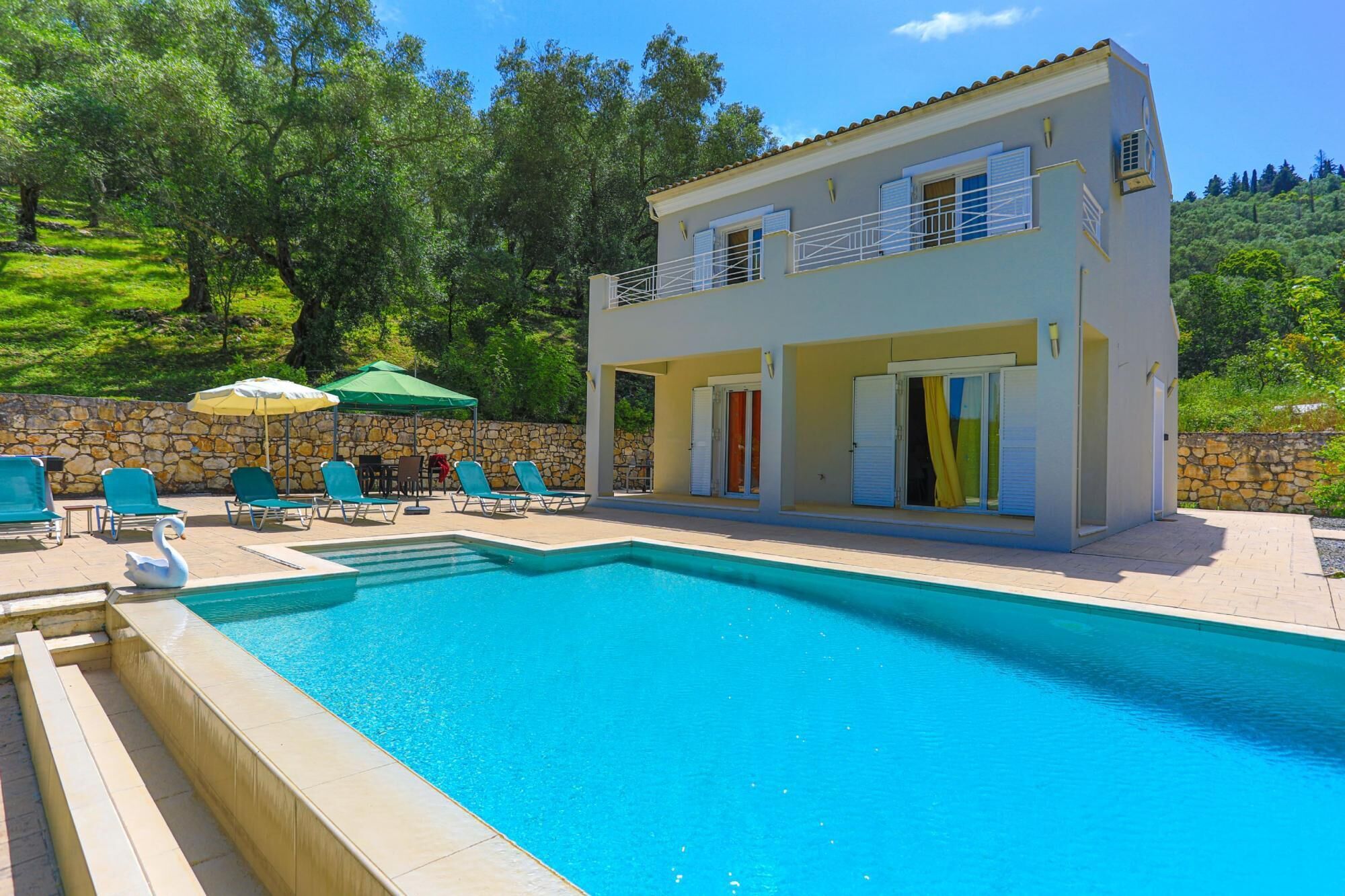 A two-story building with a swimming pool, outdoor seating, and a stone wall.