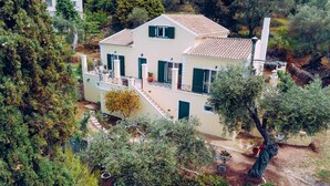 Una casa de dos pisos amb teulada de rajola, persianes verdes i un balcó.
