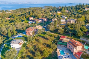 An aerial view of a residential area with houses, a swimming pool, and a view of the sea.