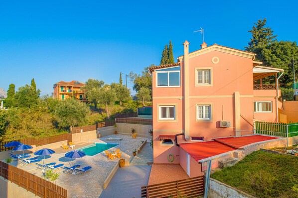 A two-story building with a swimming pool, outdoor seating, and a red-roofed terrace.