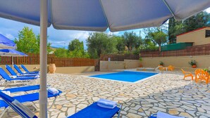 A pool area with blue lounge chairs and umbrellas, surrounded by a stone-tiled deck. - Villa Kristefi in Kato Korakiana (Corfu)