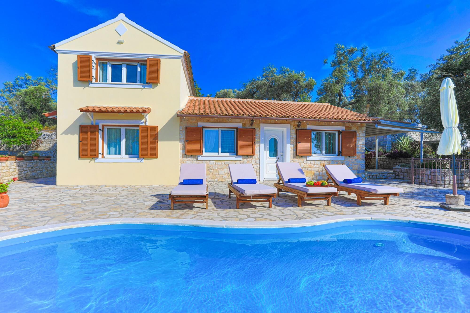 A two-story house with a swimming pool, stone walls, and wooden shutters.