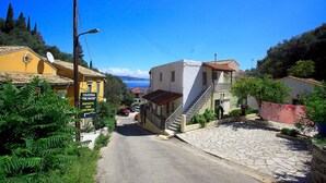 A narrow street with buildings on either side, a sign for a tavern, and a clear view of the sea in the distance. - Alexandra Apartment in Katavolos (Corfu)