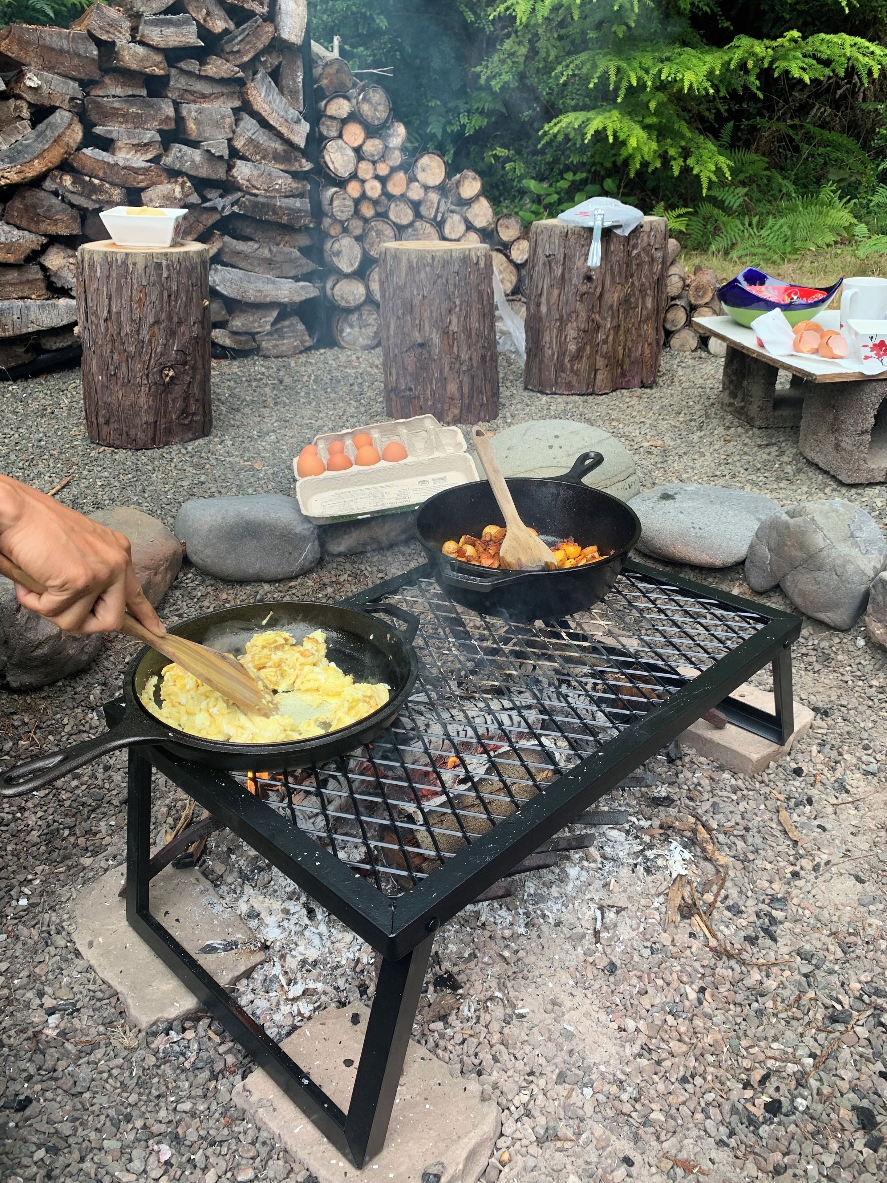 Ein tragbarer Grill mit Eiern, die im Freien zubereitet werden, umgeben von Baumstämmen und Steinen.