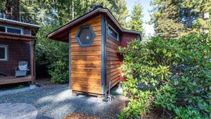 A wooden cabin with a hexagonal skylight, a porch with a chair, and a gravel pathway. - Charming Tiny House nestled in the redwoods, less than a mile from the beach. (Fort Bragg)