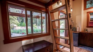 A wooden interior with a large window, a ladder, and a small kitchen area. - Charming Tiny House nestled in the redwoods, less than a mile from the beach. (Fort Bragg)