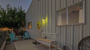 A patio area with a metal-framed bed, two turquoise chairs, and a tree.
