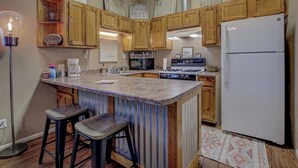 A kitchen with wooden cabinets, a central island with stools, a stove, microwave, and a refrigerator.