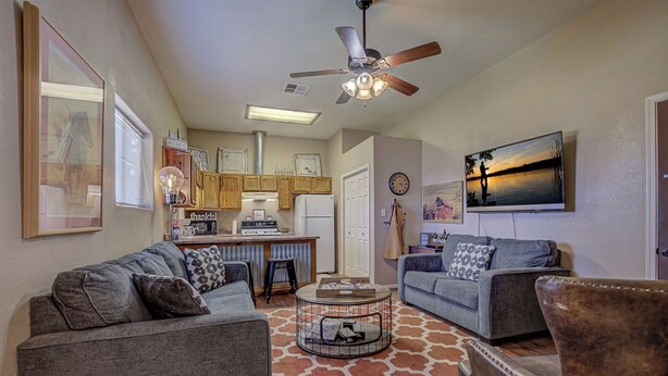 A cozy living room with two sofas, a coffee table, and a fireplace. There is a kitchen area with wooden cabinets and a dining table.