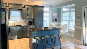 A modern kitchen with a central island, bar stools, and a view of the living area through large windows. - 4 bed/4Baths 2 mins. to ocean on golf cart -Free Waterpark with your stay! (Myrtle Beach)