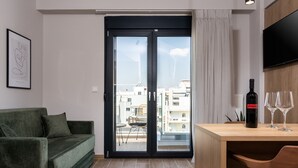 Una sala de estar moderna con un sofá verde, una mesa de comedor de madera con una botella de vino y dos copas, y un ventanal corredero que da a un balcón.