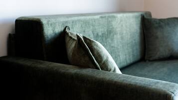 A dark green sofa with a single cushion against a plain wall.