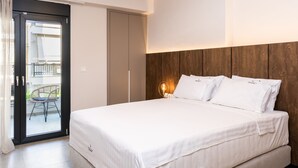 Un dormitorio con cama, cabecera de madera, mesita de noche con lámpara y puerta corrediza que da a un espacio exterior con una silla.