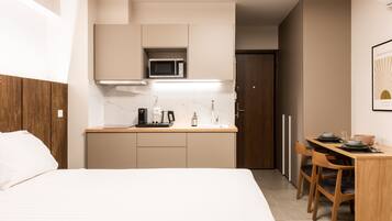A compact hotel room with a bed, a kitchenette, a dining area, and a door leading to a bathroom.