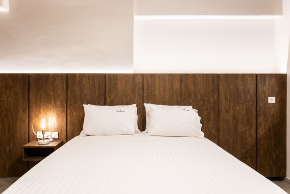 A neatly made bed with white linens, a wooden headboard, and a bedside lamp. - Empress Luxury Residences (Volos)