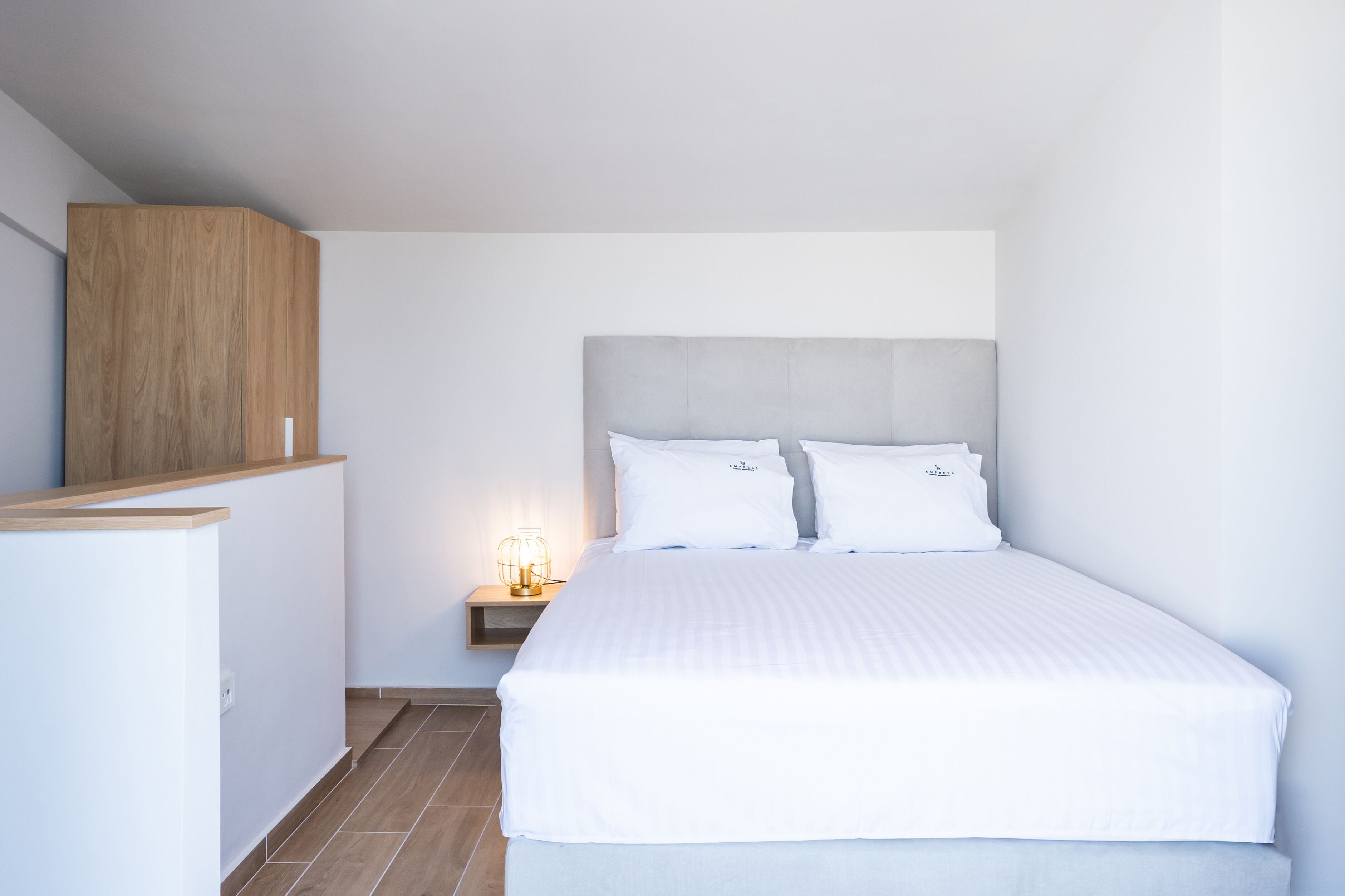 A neatly arranged bedroom with a bed, a bedside table with a lamp, and a wooden wardrobe.
