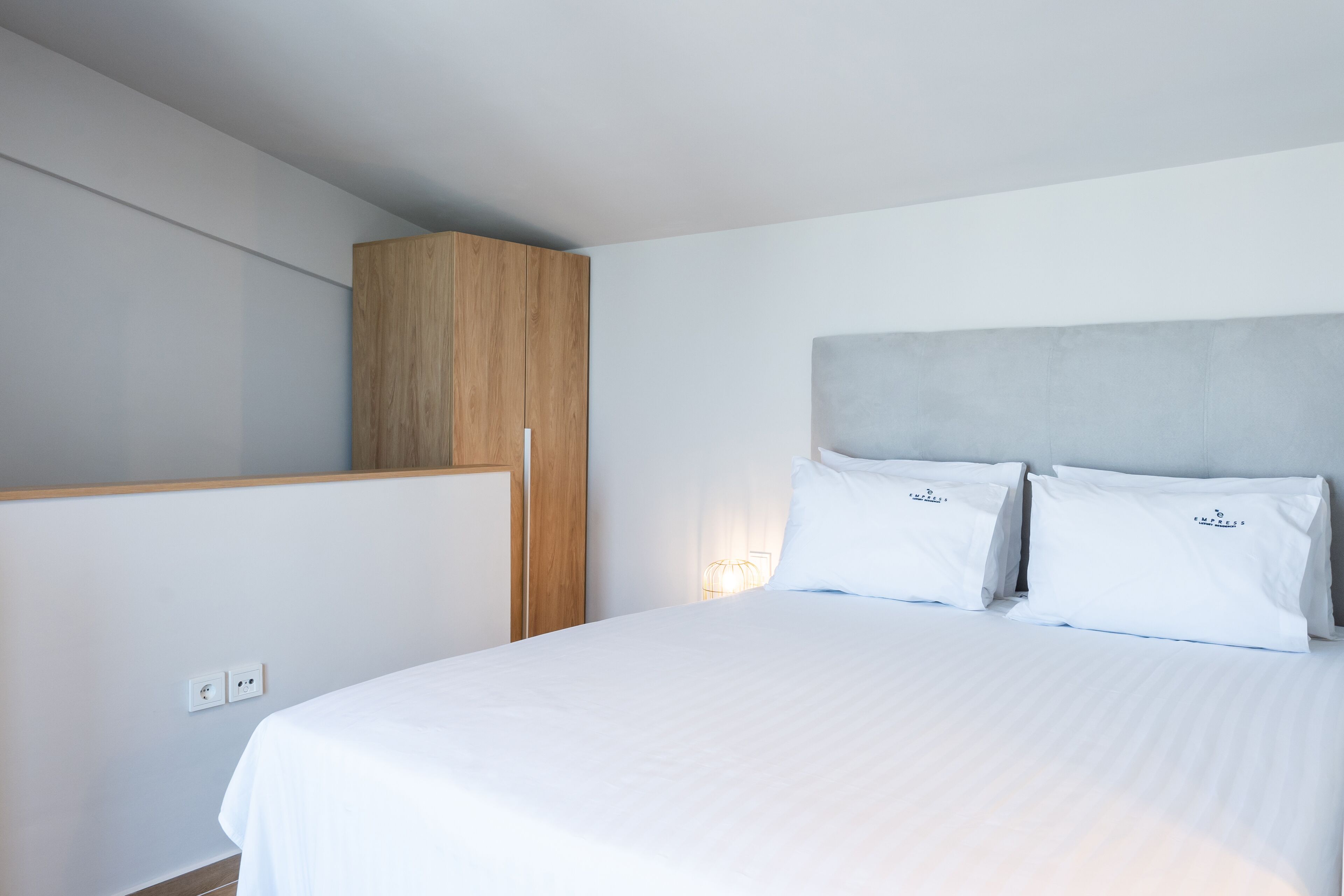 A modern hotel room with a large bed, a wooden wardrobe, and a wall-mounted light fixture.