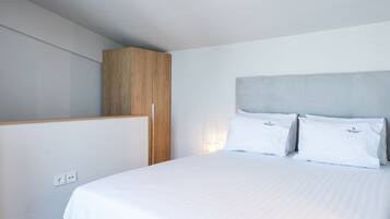 A modern hotel room with a large bed, a wooden wardrobe, and a wall-mounted light fixture.