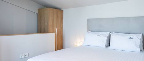 Ein modernes Hotelzimmer mit einem großen Bett, einem Holzschrank und einer wandmontierten Lampe.
