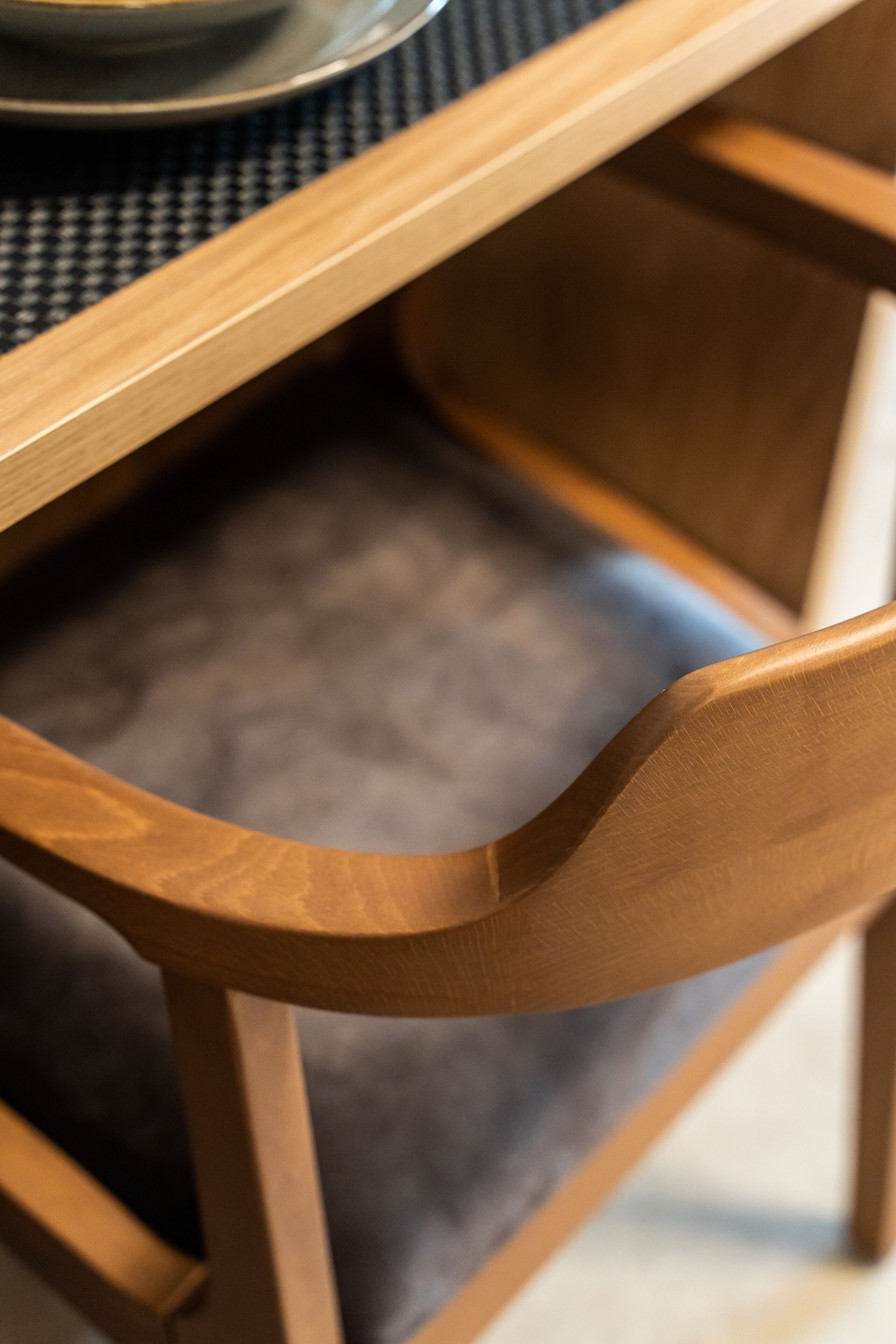 A close-up of a wooden chair with a curved backrest and a grey cushion.