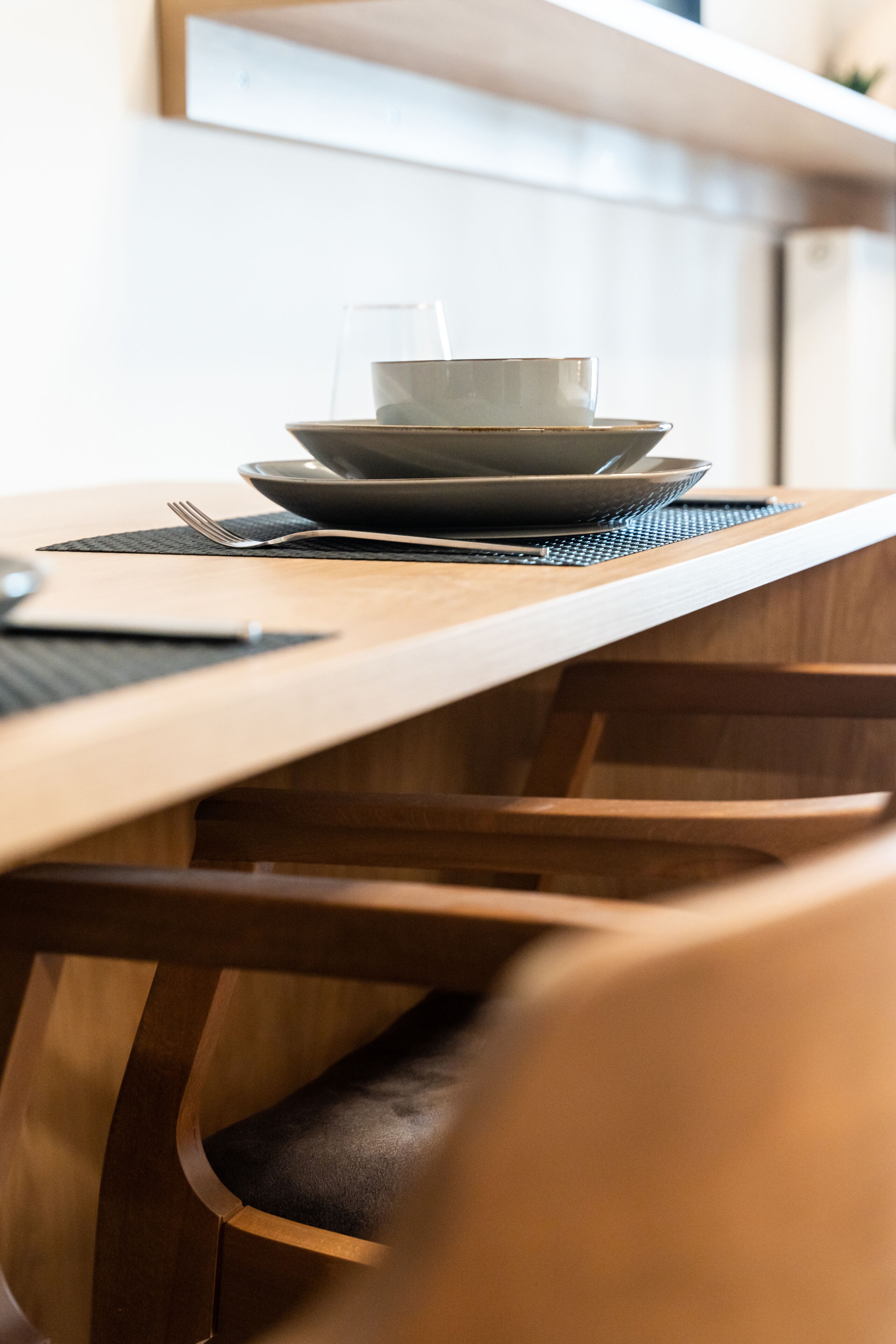 A wooden dining table with a glass and a bowl on it, a fork, and a placemat.