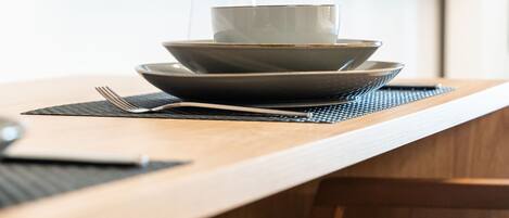 A wooden dining table with a glass and a bowl on it, a fork, and a placemat.