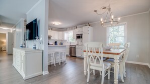 Une cuisine moderne avec des meubles blancs, un coin repas avec des chaises blanches et un lustre.