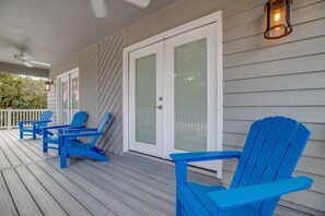 A covered porch with blue Adirondack chairs, white doors with glass panels, and a ceiling fan.