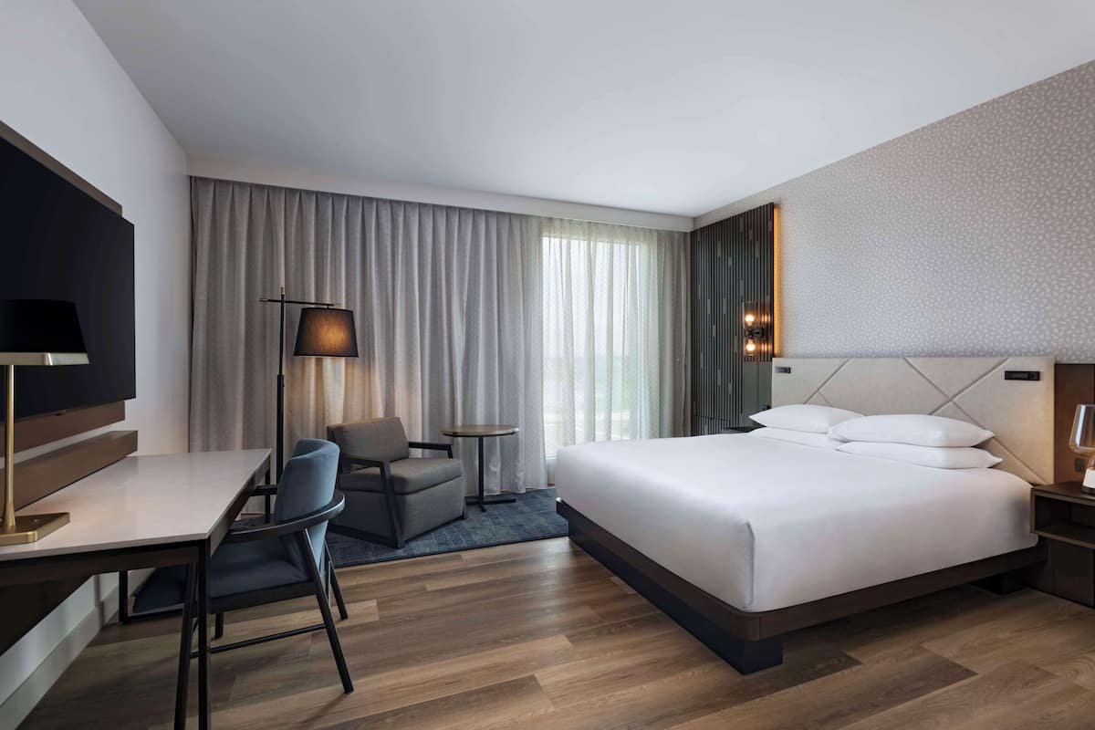 A hotel room with a large bed, a desk with a chair, a small table, and a TV.