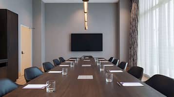 Un salón de conferencias con una larga mesa, sillas, un televisor de pantalla plana y un amplio ventanal con cortinas.