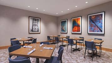 A conference room with multiple tables and chairs, framed artwork on the walls, and a patterned carpet.