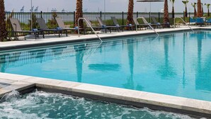 A swimming pool with lounge chairs and umbrellas, surrounded by palm trees. - Hyatt Regency Baytown-Houston (Baytown)