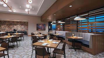 A modern restaurant with multiple dining areas, including booths and tables, and a large wall of wine bottles.