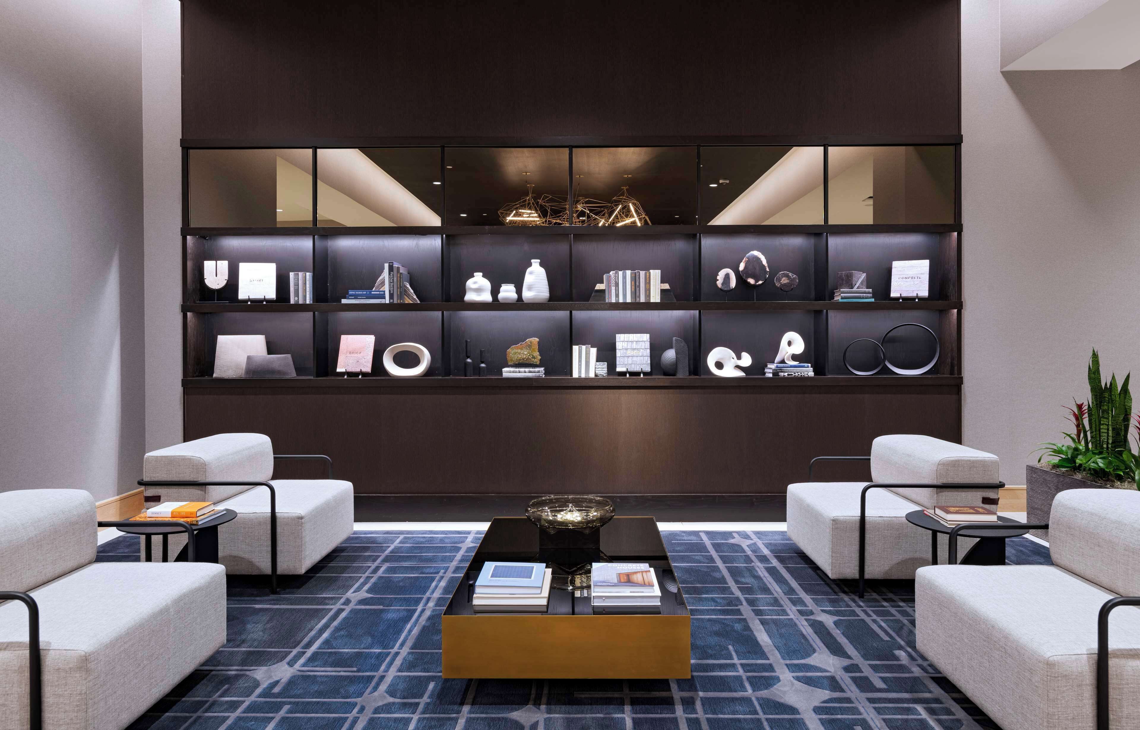 A modern lobby with a dark wood bookshelf, two sofas, a coffee table, and a patterned carpet.