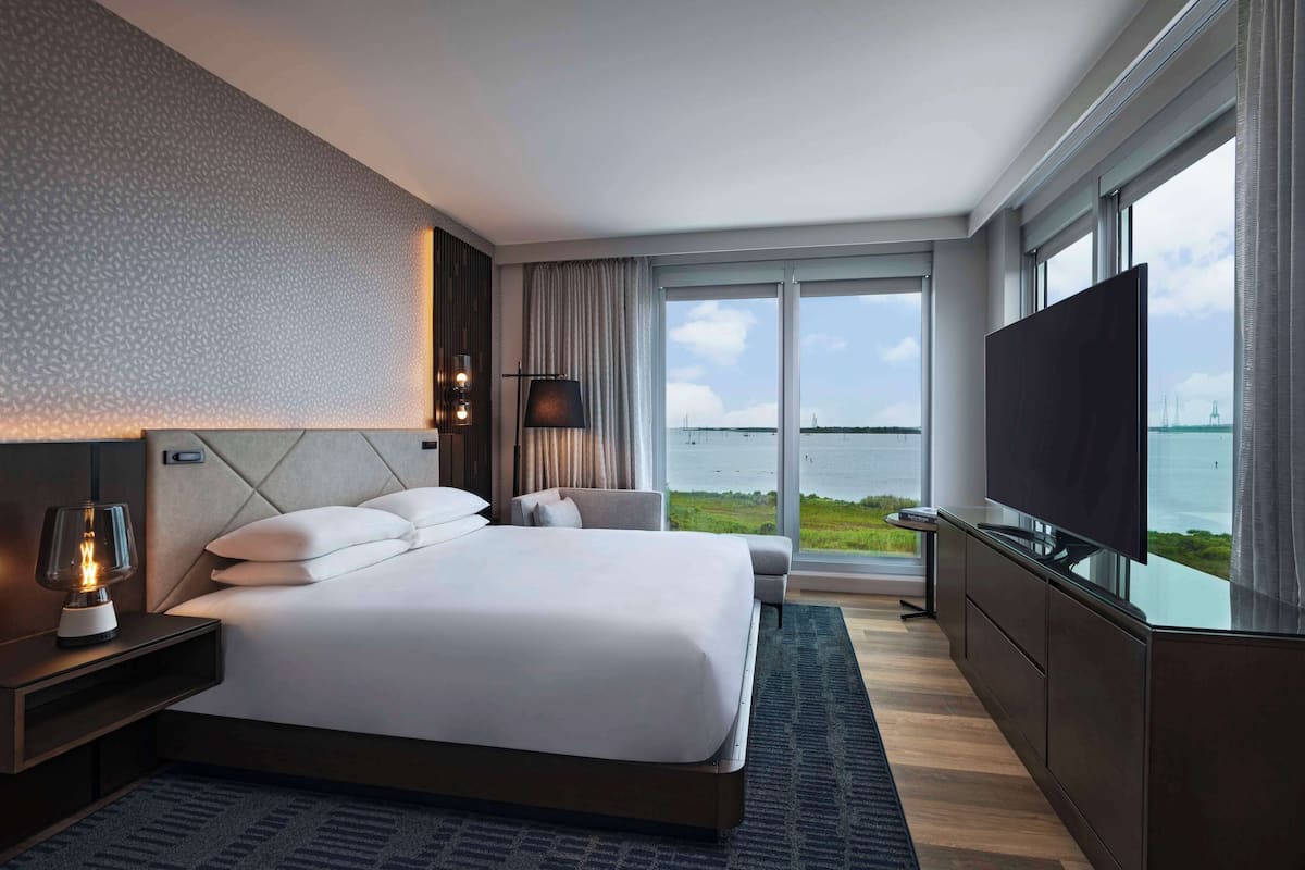 A modern hotel room with a large bed, a TV, and a view of the water.