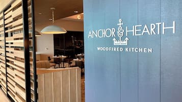 Interior de un restaurante con diseño moderno, que incluye un separador de madera y un letrero que dice 'Anchor & Hearth Woodfired Kitchen'.