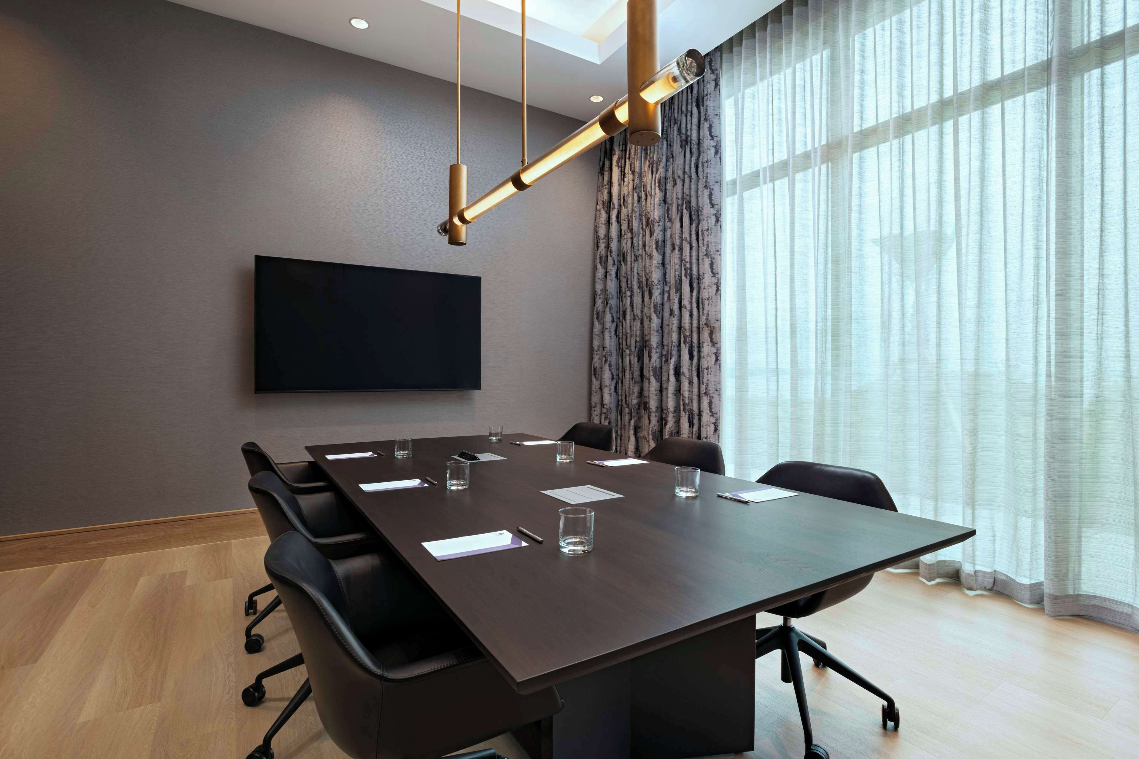A conference room with a large table, chairs, a flat-screen TV, and a modern chandelier.