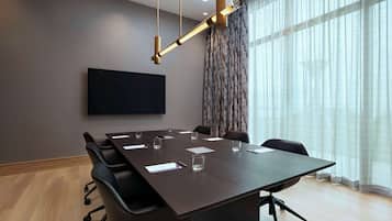 A conference room with a large table, chairs, a flat-screen TV, and a modern chandelier.
