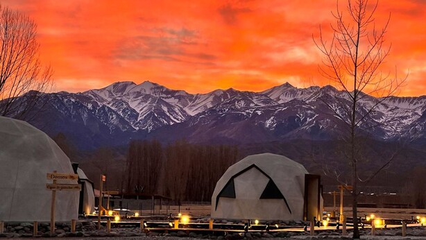 A mountain lodge with snow-covered peaks in the background, a dome-shaped building, and a wooden fence. - Cinco Cumbres luxury Camp & Eco Lodge (Uspallata)